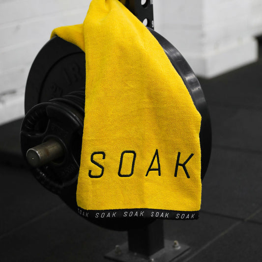 Yellow towel with 'SOAK' text draped over a barbell on a gym floor.